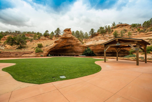 A grassy area with a stone backdrop and a wooden gazebo under a cloudy sky.